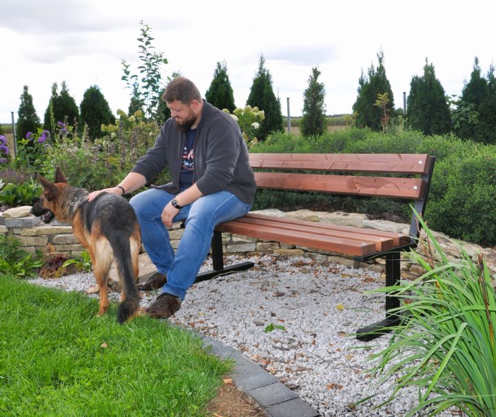 Mężczyzna siedzi na ławce w ogrodzie z psem.