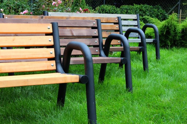 Holzbänke mit schwarzen Metallarmlehnen in einer Gartenumgebung
