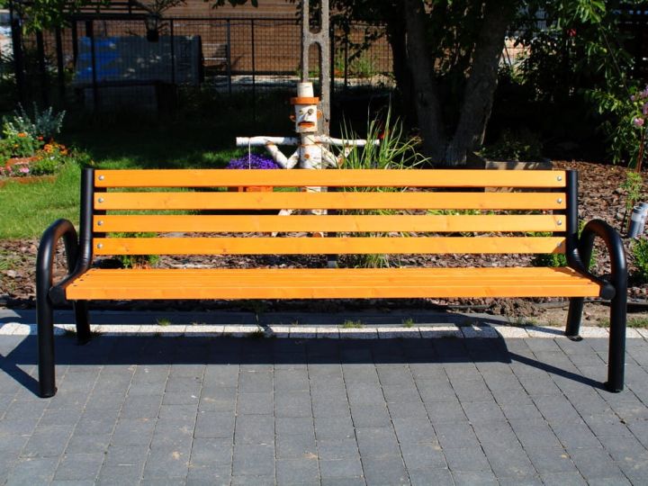 Holzbank mit Metallbeinen auf gepflastertem Gehweg